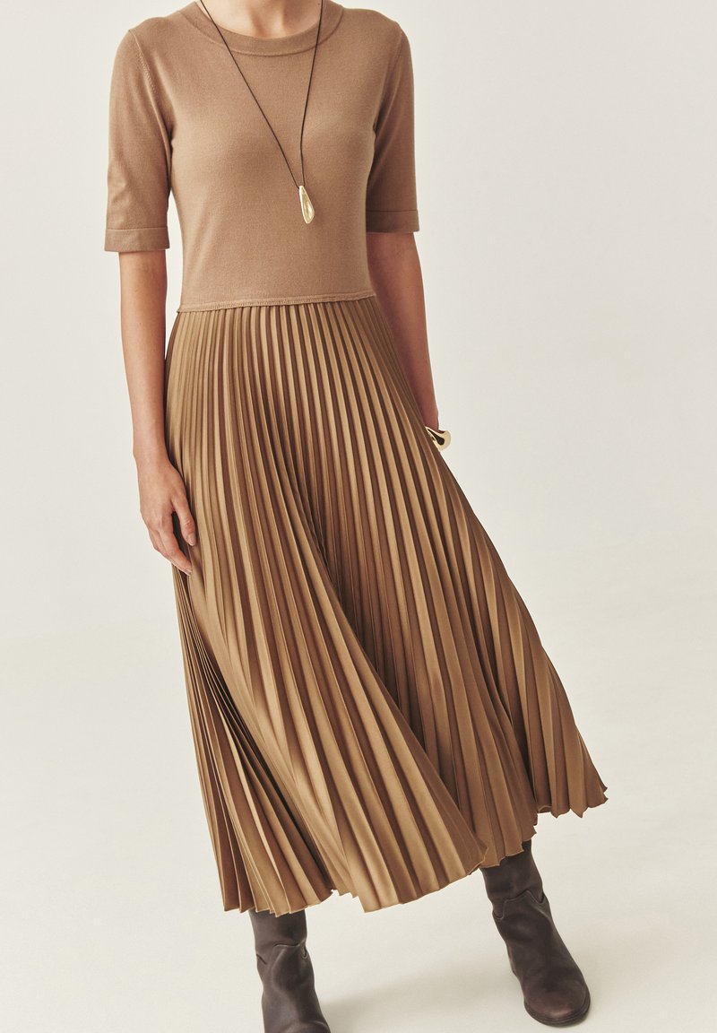 Vestido marrón plisado con mangas cortas, torso de punto y falda fluida. Cuenta con una textura suave y una silueta acampanada y en capas.