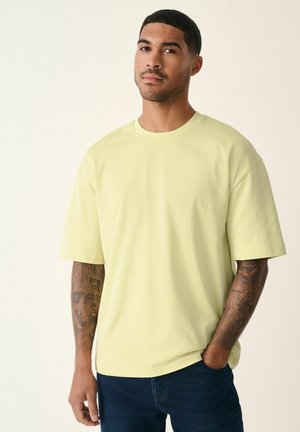 Kurzärmliges T-Shirt mit Rundhalsausschnitt aus hellgelber Baumwolle. Hat eine lockere Passform und eine glatte Textur. Wird mit dunklen Jeans getragen.