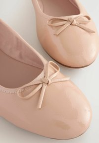 Vaaleanpunaiset kiiltäväpintaiset ballerinat, joissa on pyöreä kärki, etuosassa koristeellinen nauha ja pehmeä vuori. Sujuva rakenne ja minimalistinen muotoilu.