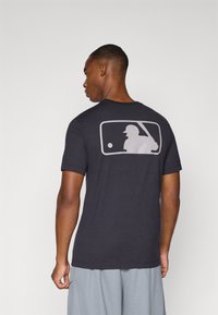 Black cotton t-shirt with short sleeves, featuring a gray MLB logo silhouette on the back. Soft texture and standard fit design.