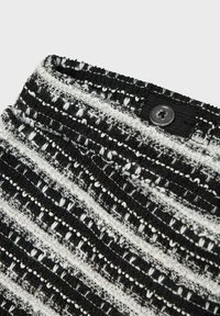 Tessuto testurizzato in bianco e nero con un motivo a strisce, che presenta un dettaglio con bottone nella parte superiore. Il materiale sembra tessuto con una finitura morbida.