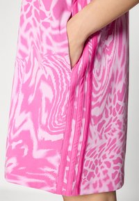 Pink patterned sports dress with a smooth texture, featuring an abstract design and side pockets. Details include triple pleats on the sides.