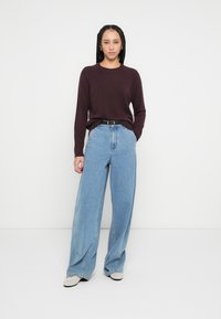 Bordo pulover z okroglim izrezom, kombiniran s svetlo modrimi kavbojkami širokih hlačnic. Obleka vključuje črni pas in priložnostne čevlje.