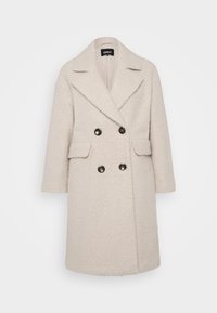 Διπλής όψης, κρέμ χρώματος παλτό με υφασμάτινη υφή. Διαθέτει μερικά καμπυλωτά κολάρα, δύο μπροστινές τσέπες και μαύρα κουμπιά.