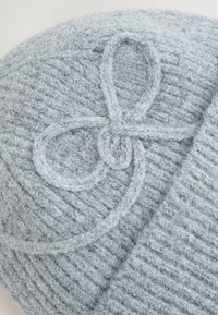 Gorro tejido gris con un patrón texturizado y un detalle decorativo de lazo de hilo gris en la parte delantera. Material suave, cálido y acogedor.