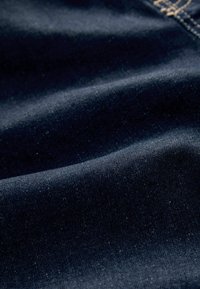 Tmavomodrý denímový materiál s hladkou textúrou, s jemnými fľakmi od vláken a prirodzenými záhybmi, ktorý má strednú hmotnosť.