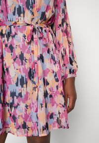 Lehká šaty s dlouhými rukávy a abstraktním vzorem v růžové, oranžové, modré a černé barvě, s uvázaným páskem v pase.
