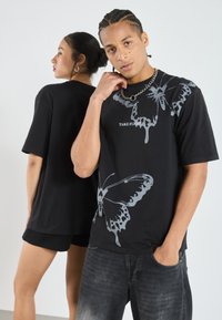 Sort t-shirt med stort gråt sommerfuglemotiv og teksten "TAKE FLIGHT". Korte ærmer, afslappet pasform, parret med denim og shorts.