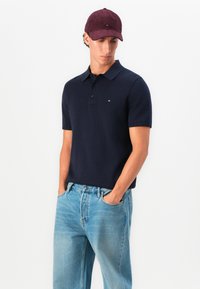 Námořní polo tričko s krátkými rukávy a límečkem, spárované s světle modrými džíny. Burgundská sametová kšiltovka s malým logem.