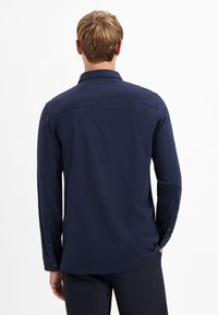 Marineblauw overhemd met lange mouwen, een gladde textuur, knoopmanchetten en een klassieke kraag. Achteraan heeft het een rechte zoomlijn.