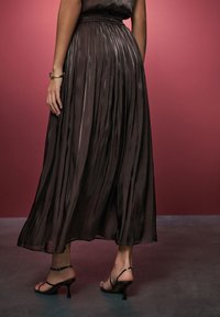 Plissierter schwarzer Maxirock mit glatter, fließender Textur, tailliertem Bund, kombiniert mit Riemchen-Pumps, Rückansicht.