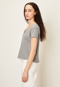 Pilkas trumpas rankovėmis marškinėliai su V formos iškirpimu, pagaminti iš minkštos medžiagos, dailiai pasiųti ir su šiek tiek trumpesne forma. Derinami su baltais džinsais.