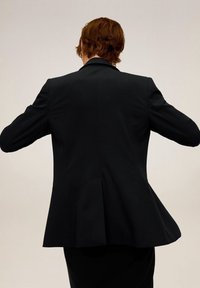 Blazer negro ajustado, hecho de una tela suave, que presenta un corte entallado en la parte trasera y un dobladillo acampanado, con hombros estructurados y un diseño limpio.