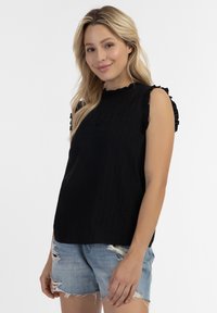 Top nero senza maniche con design a spalle arricciate e tessuto testurizzato, abbinato a pantaloni corti di jeans strappati. Stile semplice e casual.