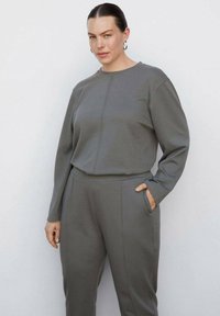 Grijze hoodie en bijpassende broek van een gestructureerde stof. De top heeft lange mouwen, een ronde hals en een naaddetail aan de voorkant.