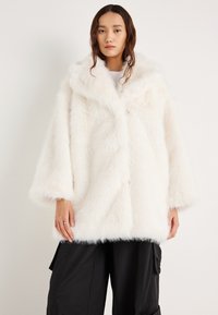 Παλτό από λευκή συνθετική γούνα με φαρδιά γιακά, άνετη εφαρμογή και μανίκια μέτριου μήκους. Η απαλή υφή και τα διακριτικά κουμπιά δημιουργούν ένα μινιμαλιστικό σχέδιο.