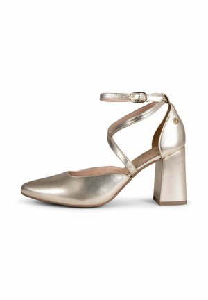 Zapato de tacón alto dorado metálico con punta puntiaguda, correas que envuelven el tobillo y tacón cuadrado sobre fondo blanco.
