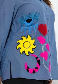 Camicia blu button-up con vivaci ricami: un occhio, un cuore, un sole e motivi floreali con texture in rosso, giallo, rosa e nero.