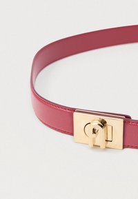 Sarkans ādas josta ar gludu tekstūru, tam ir zelta taisnstūra sprādze un unikāls aizslēgšanas mehānisms aizvēršanai.