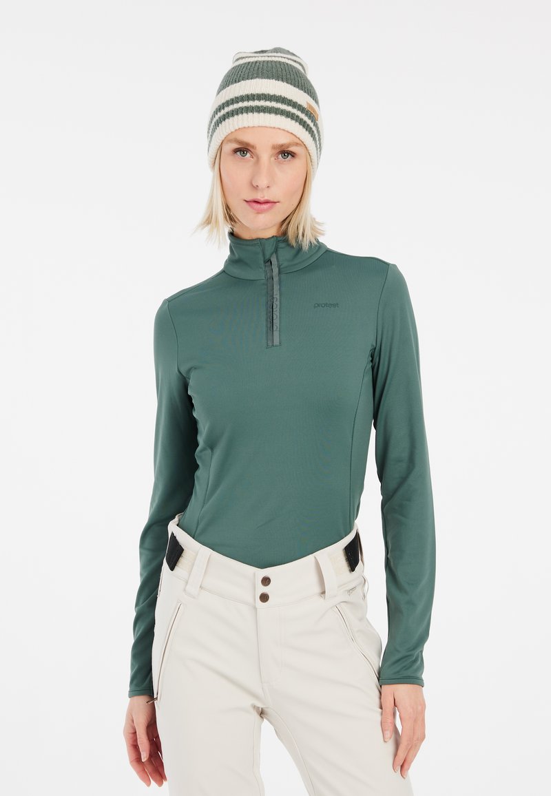 Maglia verde a maniche lunghe con zip realizzata in tessuto morbido, abbinata a pantaloni chiari e un berretto in maglia a righe multiple.