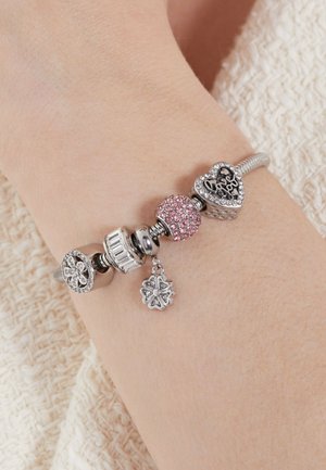 Silver charm bracelet featuring various beads: a pink crystal bead, a heart-shaped charm, and floral accents on a flexible band.