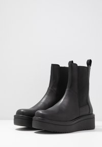 Botine negre din piele cu panouri elastice laterale, talpă groasă și bucle pentru o purtare ușoară. Textură netedă și design elegant.