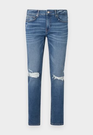 Kék, slim-fit farmernadrág, szakadt részekkel mindkét térdnél, öt zsebes kialakítás, gombos záródással a deréknál, fehér háttéren laposan elterítve.