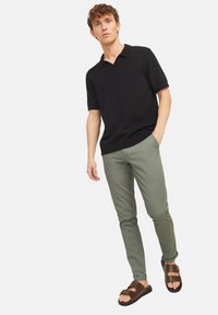 Polo shirt noir à manches courtes, pantalon vert et sandales marron. Le polo présente un col simple et une coupe décontractée. Textures lisses tout au long.