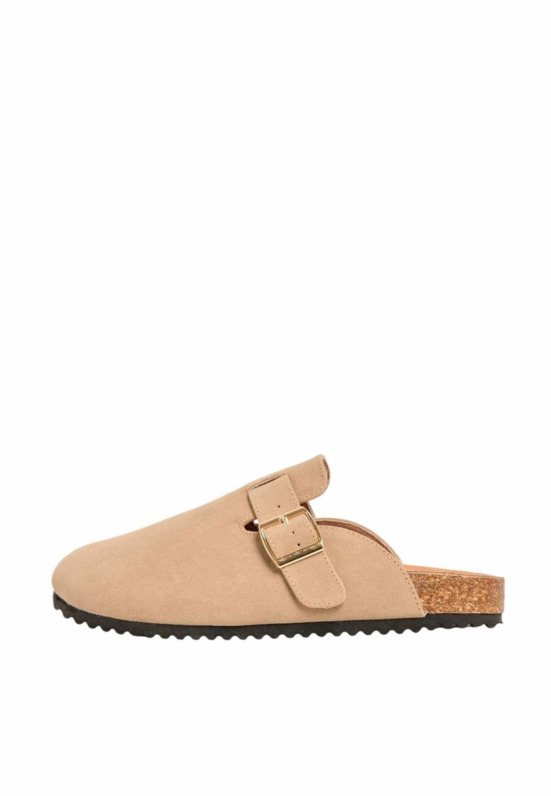 Beige suede sussumma, mille korkpõhjaga, metallist kinnitusriba ja ümarate varvastega. Tekstuuriga pind ja kontuuritud profiil.