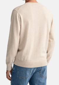 Beiger Strickpullover von hinten betrachtet, mit Rundhalsausschnitt, gerippten Bündchen und Saum sowie einer glatten Textur. Kombiniert mit blauen Jeans.