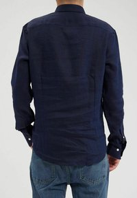 Chemise à manches longues bleu marine en lin. Dotée d'un col standard et de poignets à bouton, avec une texture lisse et un design ajusté.