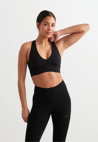 Svart sports-bh med dyp V-hals, støttende design og glatt tekstur. Kombinert med høytlivs svarte leggings, begge laget av elastisk stoff.