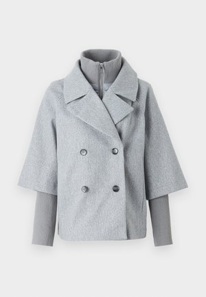 Hallikas topeltklappidega jope laiad kraed, lühikesed varrukad ja soonikkoes kõrge kaelus. Omab kahte tumedat nööpi ja tekstureeritud kangast.