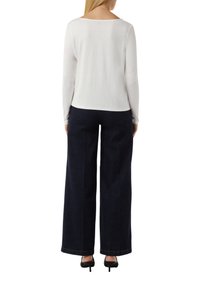 Weißes Langarmoberteil mit rundem Ausschnitt, kombiniert mit dunkelblauen, weit geschnittenen Jeans. Schwarze Absatzschuhe runden das Outfit ab.