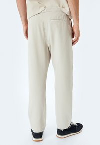 Pantaloni beige chiaro con una vestibilità comoda, gambe dritte, dettagli sulle tasche posteriori e una texture morbida. Abbinati a scarpe sportive scure.