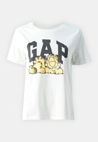 Bílá bavlněná tričko s velkým černým logem "GAP" a grafikou spícího kresleného kocoura v žluté a hnědé barvě. Krátké rukávy.