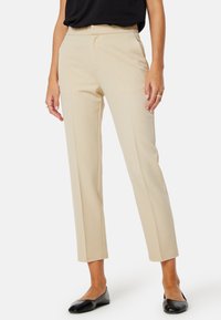 Beige op maat gemaakte broeken met een rechte pijp, een gladde textuur en subtiele details in de voornaad, gecombineerd met zwarte flats.