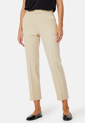 Beige op maat gemaakte broeken met een rechte pijp, een gladde textuur en subtiele details in de voornaad, gecombineerd met zwarte flats.
