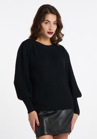 Maglione nero lavorato a maglia con scollatura rotonda e maniche a sbuffo, design testurizzato, abbinato a una gonna di pelle nera.