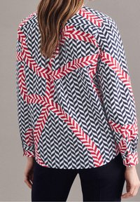 Långärmad blus med ett marinblått och vitt chevronmönster samt röda randiga detaljer. Tillverkad av ett lätt material med en avslappnad passform.