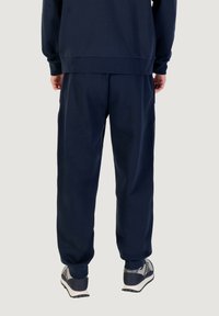 Dunkelblaue, locker sitzende Jogginghosen aus weichem Stoff, mit elastischen Bündchen und Bund, kombiniert mit grauen Sportschuhen.
