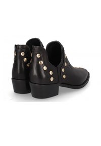 Botas de tobillo de cuero negro con un tacón bajo, que presentan remaches redondos dorados en los lados exteriores y un diseño elegante y minimalista.