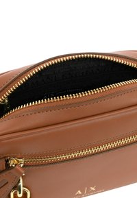 Borsa in pelle marrone con una zip dorata, dotata di una fodera interna nera con un logo. Design slim con una tasca con zip.