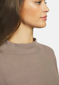 Pull en rib de couleur brun clair avec un col rond haut. Texture douce, design ajusté. Mettez l'accent sur les détails du cou et des épaules en vue de profil.
