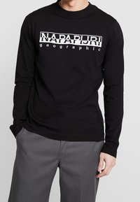Long-sleeve black cotton t-shirt with white graphic text "NAPAPURI" and "geographic" across the chest. Crew neckline and fitted style.