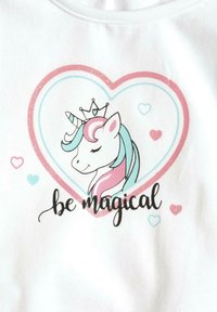 Biała bawełniana koszulka z grafiką jednorożca w różowo-turkusowej kolorystyce, otoczona sercem i napisem "bądź magiczny".