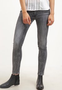 Jeans ajustados en denim gris desgastado, con una textura suave, un ligero desgaste y costuras clásicas. Combinados con botas negras por el tobillo.