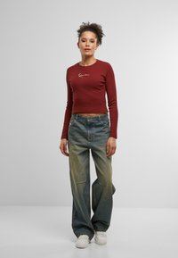 Maroon cropped long-sleeve top with white embroidered detail, paired with loose-fit, faded blue jeans, and white sneakers.