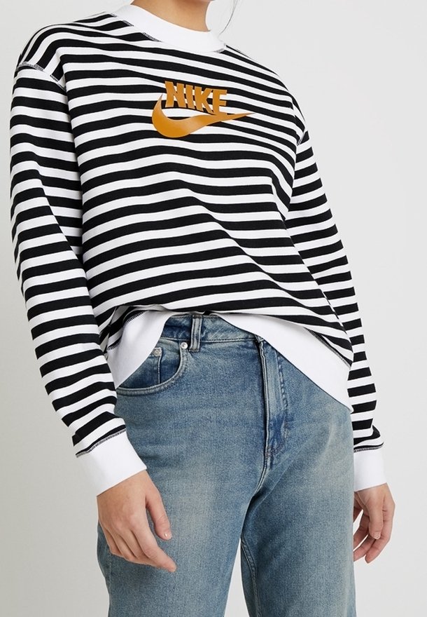 Svart- och vitrandig sweatshirt med rund halsringning, prydd med en orange Nike-logga. Tillsammans med ljusblå denimjeans.
