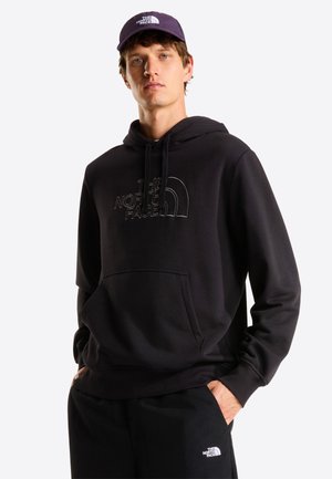 Felpa nera con cappuccio, tasca frontale e logo ricamato. Abbinata a pantaloni neri. Il modello indossa un cappello nero abbinato con logo.